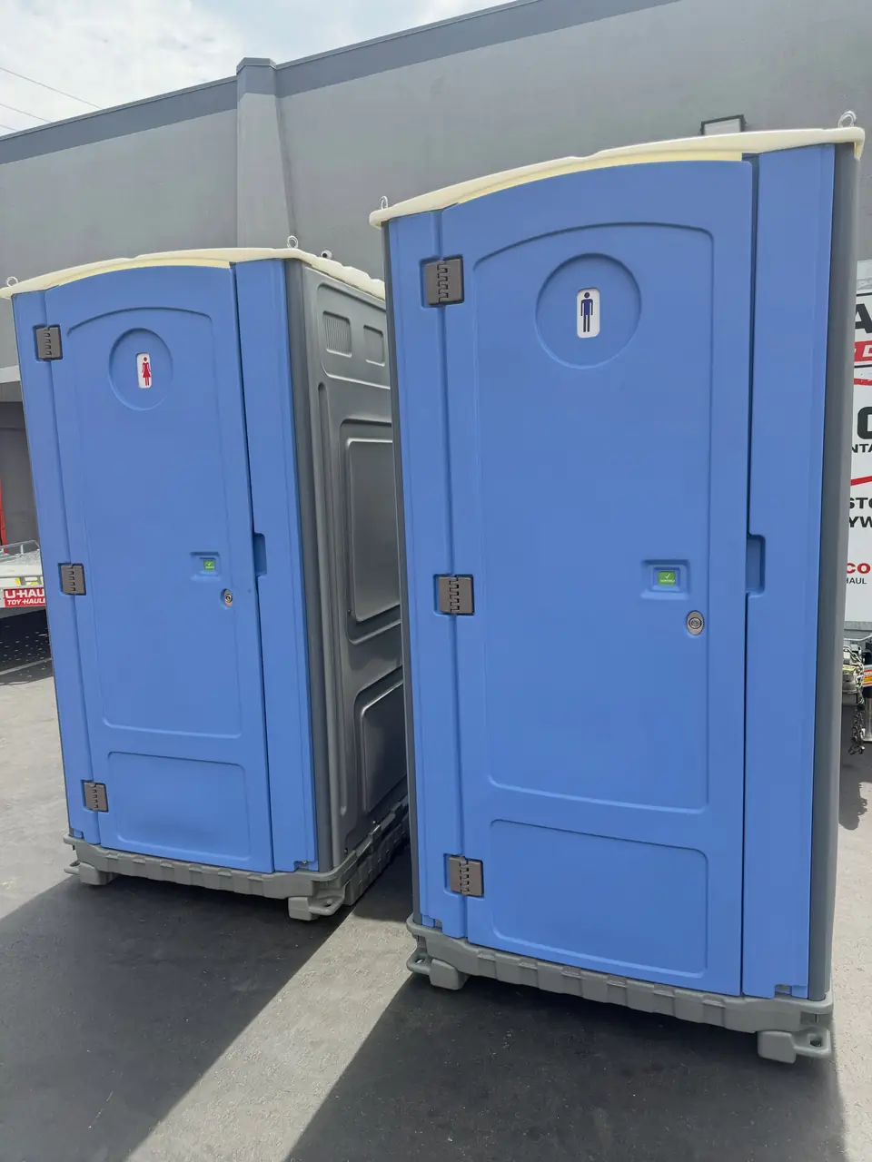 Two blue porta potties in a paved parking area